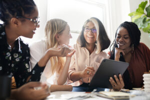 Four women of diverse ethnicities having a meeting using a digital tablet to create inclusive social media strategy.